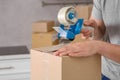 Man taping box with adhesive tape dispenser in kitchen, closeup Royalty Free Stock Photo