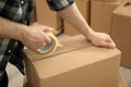 Man taping cardboard box indoors, closeup view