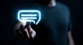 Man taps glowing chat bubble icon representing online communication and digital interaction on dark background Royalty Free Stock Photo