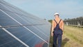 Man technician in hard hat walks on new ecological solar construction outdoors. Farm of solar panels. Maintenance