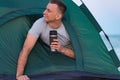 Man in tent with tourist mug in his hands. Camping morning. Active tourism