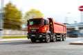 MAN TGS 41.440 tipper truck is driving in city on high speed. Dump truck MAN with red cabin at the city highway in motion