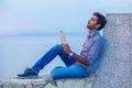 Man thinking using pad sitting on a concrete bridge above the sea