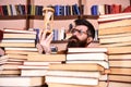 Man on thoughtful face holds hourglass while studying, bookshelves on background. Man, scientist in glasses looks at Royalty Free Stock Photo