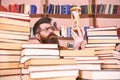 Man on thoughtful face holds hourglass while studying, bookshelves on background. Man, scientist in glasses looks at Royalty Free Stock Photo