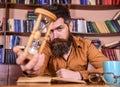 Man on thoughtful face holds hourglass while studying, bookshelves on background. Self education concept. Man sits at Royalty Free Stock Photo