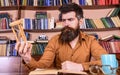 Man on thoughtful face holds hourglass while studying, bookshelves on background. Teacher or student with beard studying Royalty Free Stock Photo