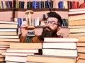 Man on thoughtful face holds hourglass while studying, bookshelves on background. Teacher or student with beard studying Royalty Free Stock Photo