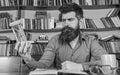 Man on thoughtful face holds hourglass while studying, bookshelves on background. Teacher or student with beard studying Royalty Free Stock Photo