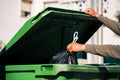 Man throwing out black eco-friendly recyclable trash bag in to big plastic green garbage container. Take out the trash Royalty Free Stock Photo