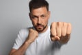 Man throwing punch against grey background, focus on fist. Space for text