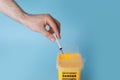 Man throwing used syringe into sharps container on light blue background, closeup