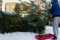 A man throws an old Christmas tree, which he brought on a plastic sleigh to waste containers.