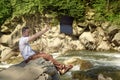 Man throws out laptop sitting at the bank of river over the waterfall. Tired from work concept Royalty Free Stock Photo