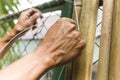 A man ties together split bamboo poles with nylon string, affixing it to a chain link fence to cover it. Home renovation and Royalty Free Stock Photo