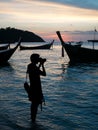 Silhouette traveller Man holding DSLR camera took a wonderful photo of boats, blue sea, and sunset at beach