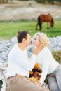 Man touches his hand to woman's cheek while sitting on a blanket. Brown horse grazing in the background Royalty Free Stock Photo