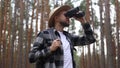 Man tourist with a backpack looks through binoculars while hiking in the forest