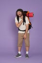 Man tourist in casual clothing with backpack standing holding shoulder looking tired. Isolated on purple background