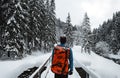 Man tourist and climber with orange backpack standing on the bridge with amazing view on snowy mountains in cold winter time.