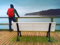 Man tourist with red backpack on wooden sea pier. Autumn rainy day. Royalty Free Stock Photo