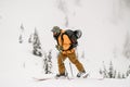 man tourist with skis and trekking poles walks up the hill against the backdrop of snow-covered trees