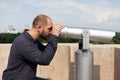 Man tourist standing on building rooftop looking through binocular telescope