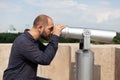 Man tourist standing on building rooftop looking through binocular telescope