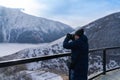 man tourist standing and taking photo of Caucasus mountains in winter from the viewpoint of Gergeti Trinity Church in Kazbegi, Royalty Free Stock Photo