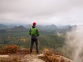 Man tourist stay on sharp rock peak. Alone hiker in red cap and green jacket enjoy view