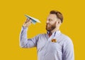 Man tourist throwing paper plane planning summer holiday trip on yellow studio background Royalty Free Stock Photo