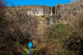 Man tourist walking on a foot path in a forest. Devil`s chimney waterfall in the background. Warm sunny day. Travel and nature