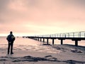 Man tourist at wooden sea pier. Cold windless morning with gradient sunlight. Smooth water