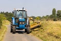 Man in a tractor using a flail to cut grass verges in a country lane. UK