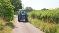 Man in a tractor using a flail to cut grass verges in a country lane. UK