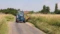 Man in a tractor using a flail to cut grass verges in a country lane. UK