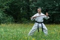 A man in a traditional kimono with a black belt trains karate kick with a bokken. Royalty Free Stock Photo