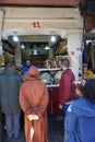 Man in traditional Moroccan monk robe and young American girl standing in life at store booth in Jemaa el-Fnaa market place in