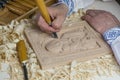 Man in traditional ukrainian clothes carves orthodox wooden icon of the Mother of God and child.