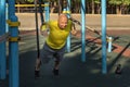 man trains with gymnastic rings on a street sports ground on a sunny day.