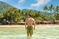 Man travel in Thailand on Tropical Koh Tao island. Person stands in sea water on Sairee beach against palms on shore