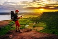 Man traveler with backpack looking at the map on edge of cliff, on a top of the rock mountain at sunset Royalty Free Stock Photo