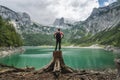 Man traveler standing on tree stump ejoying view of Dachstein peak mountains on a Upper Gosau Lake. Gosau, Salzkammergut