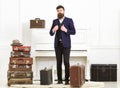 Man, traveller with beard and mustache with luggage, luxury white interior background. Macho elegant on strict face