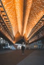 Man and a traveller in a black coat and white shoes walk through the famous Stadshall building in the centre of Ghent on