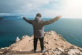 Man traveller stands on top of rock cliff with arms outstretched and looking at sea landscape, freedom of adventure concept Royalty Free Stock Photo