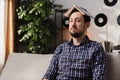 A man tries to memorize new English words. A bearded man is sitting on a couch with a dictionary open on his head