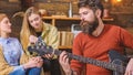 Man with trimmed beard and mustache holding electrical guitar. Musician in terracotta pullover wearing trendy watch and