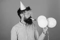 Man with trimmed beard wearing pink shirt and party cap isolated on red background. Bearded man blowing party whistle