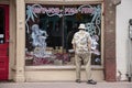 Man in tropical shirt and hat and sandals looks in painted and decorated window of closed b